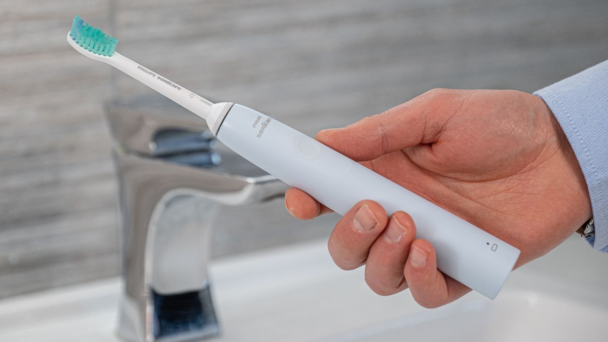 Hand holding a Philips Sonicare toothbrush over the sink.
